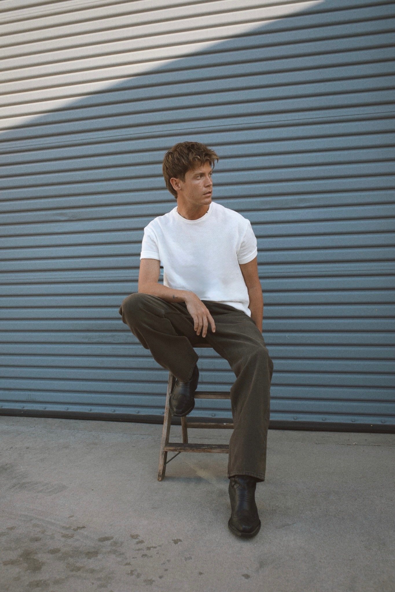 Jamie Miller seated on a wooden stool in front of a blue roller door