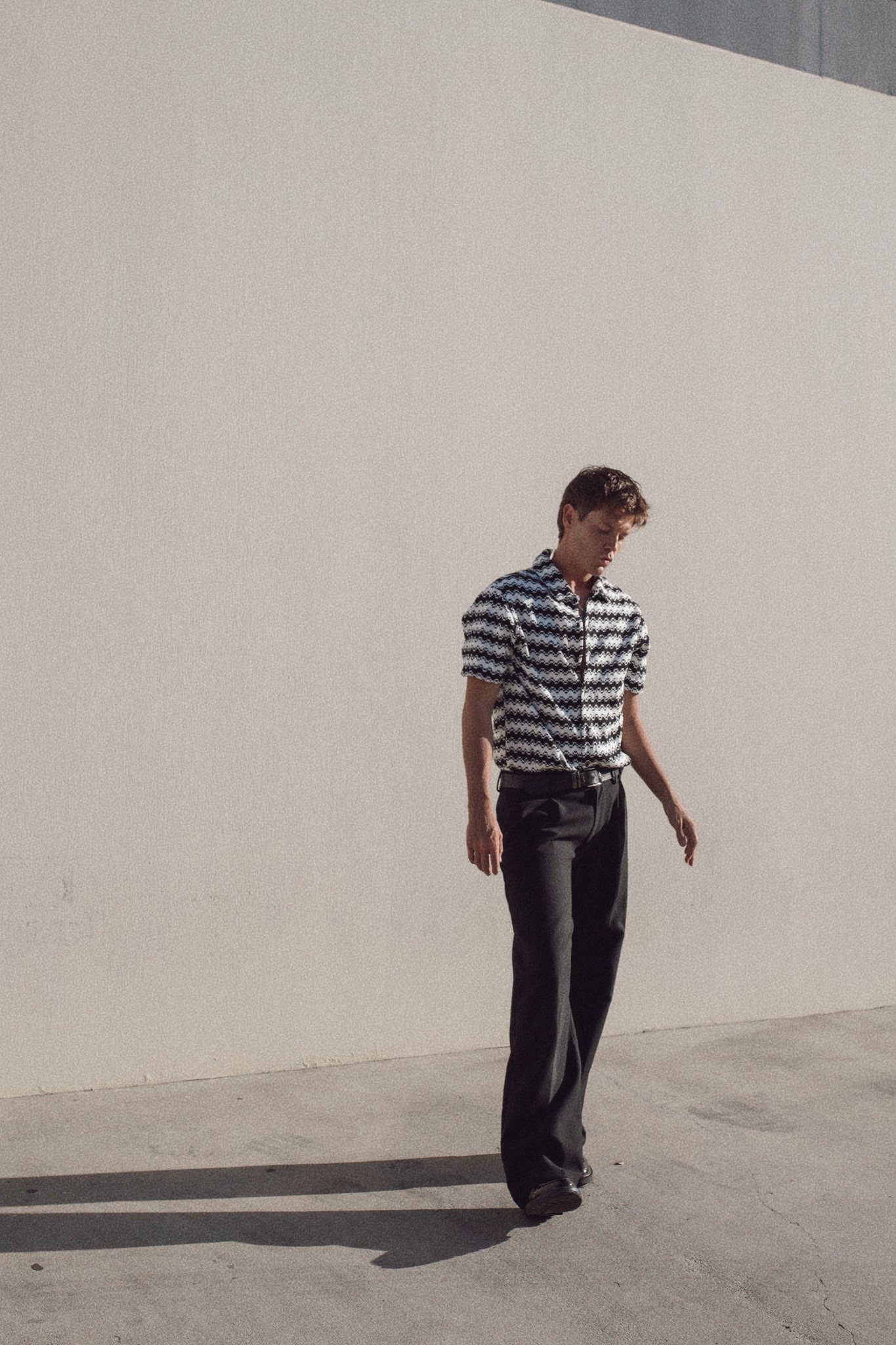 Jamie Miller walking past a white wall in a striped shirt